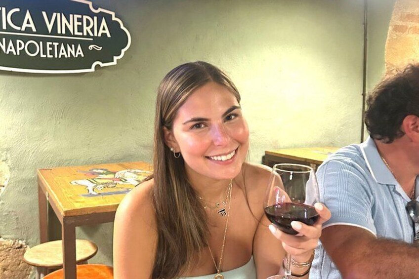 A person holding a glass of red wine, a table with a colorful tablecloth, and a sign that reads 'Napoletana.' 5
