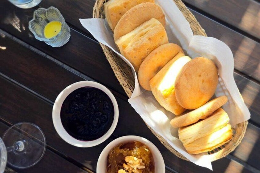 A basket of round bread rolls, a bowl of dark sauce, and a glass of wine on a wooden table. 5