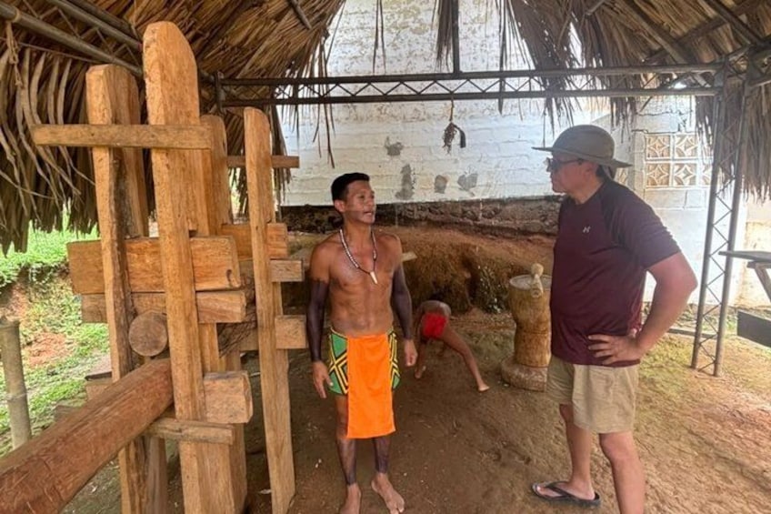 A wooden structure with a thatched roof, a person in a green and yellow outfit, and another person in a maroon shirt and beige shorts. 5
