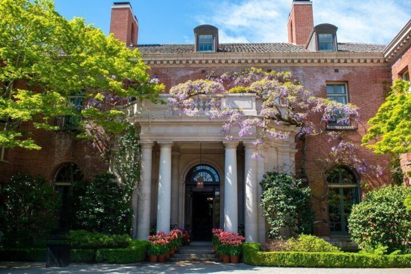 A brick building with a classical entrance, surrounded by lush greenery and flowering plants. 5