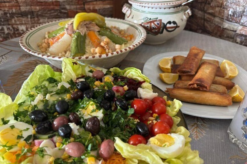 A table with a salad, a bowl of soup, and a plate of spring rolls. 1