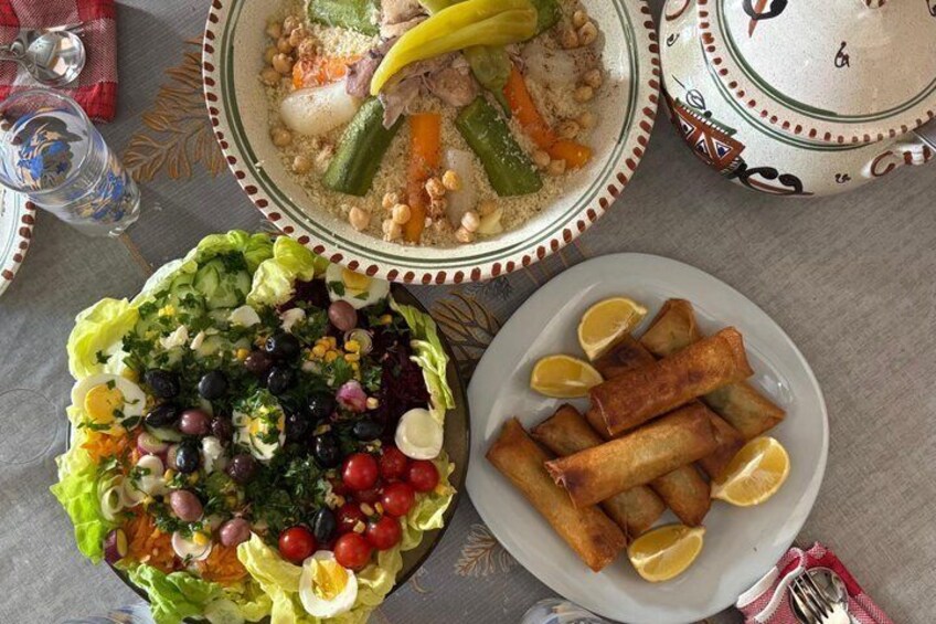 A table with a salad, a bowl of couscous, and fried spring rolls. 3