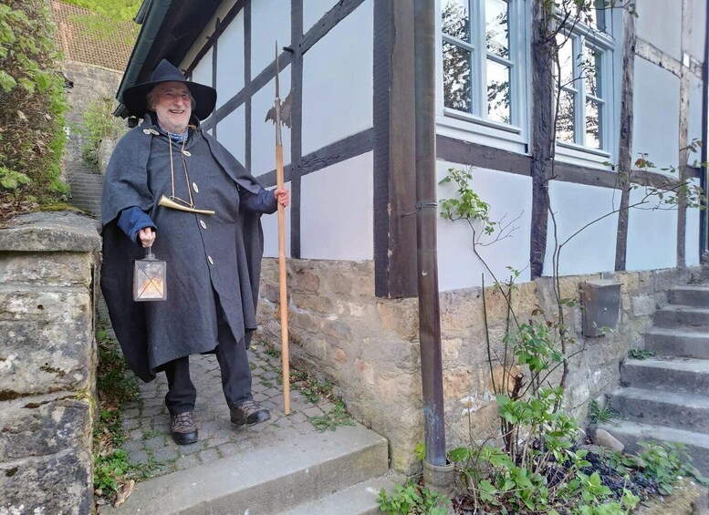 A person in historical costume standing on stone steps next to a building with exposed timber framing. 5