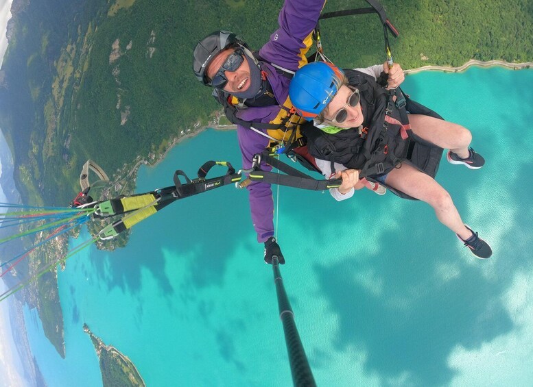 Two people skydiving with parachutes over a turquoise body of water and green landscape. 3