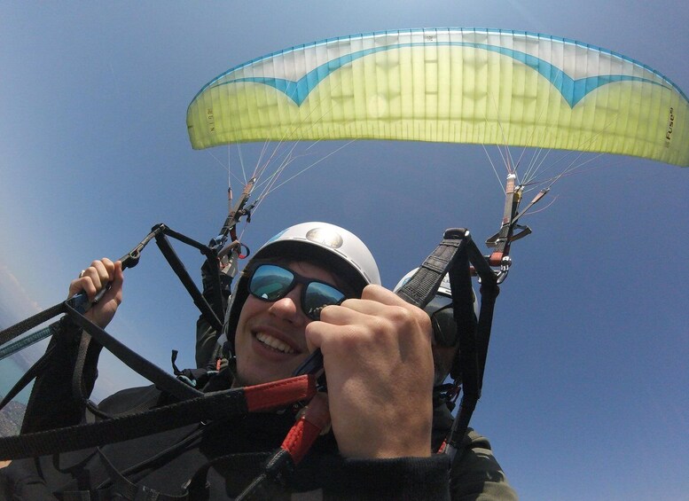 A person paragliding with a yellow and blue canopy, wearing a helmet and harness. 5