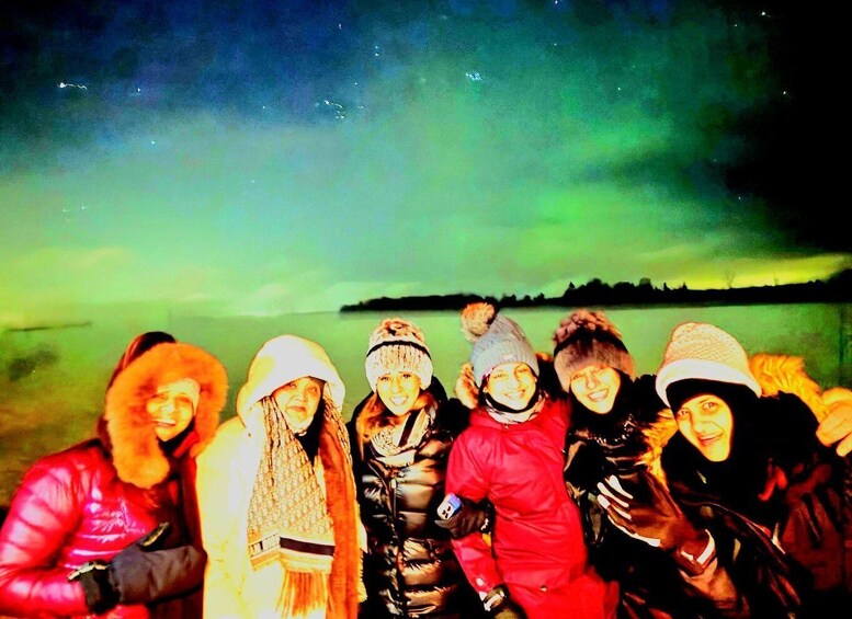 A group of people outdoors during twilight with a visible aurora borealis in the sky. 1