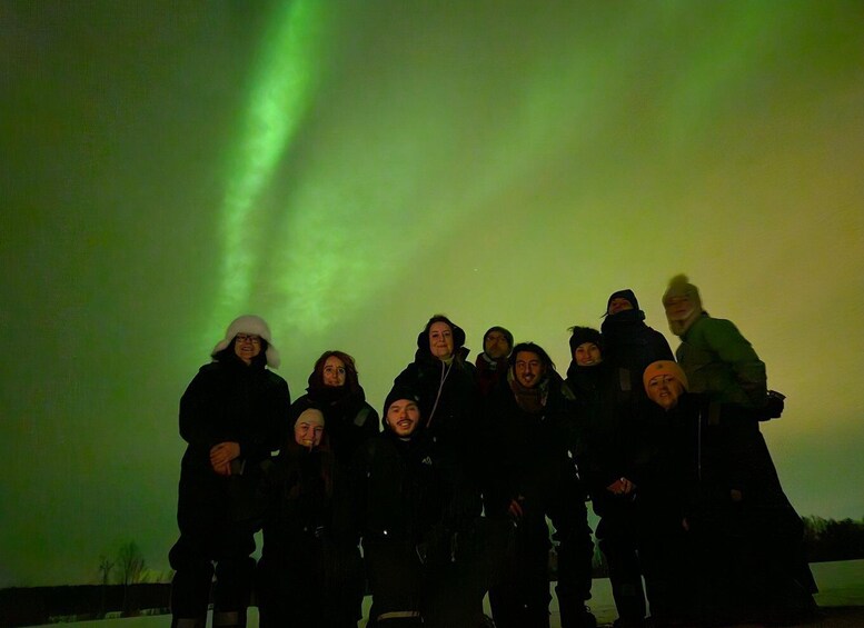 A group of people standing outdoors under a green aurora borealis. 2