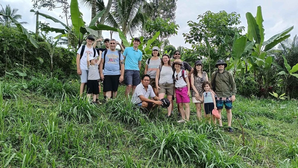 Un groupe de personnes se tient dans un champ verdoyant et luxuriant, avec de grands plants de bananiers et des palmiers en arrière-plan. 5