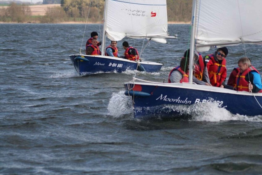 Two sailboats on a body of water with people wearing life jackets. 3