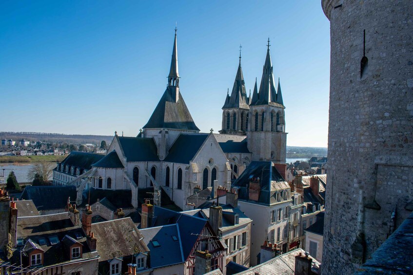 A historic town with a prominent church featuring a tall spire, a castle-like structure with multiple towers, and a river in the background. 4
