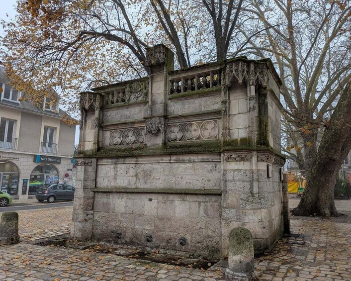 A stone monument with intricate carvings, surrounded by trees and a cobblestone path. 3