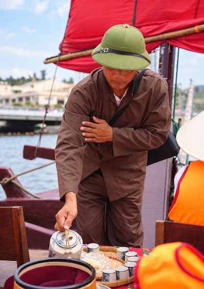 A person in a brown outfit and green hat preparing food on a boat. 5