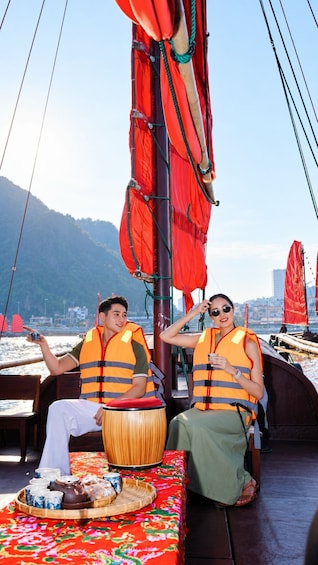 Two people on a boat wearing life jackets, a table with a teapot and cups, and a mountainous landscape in the background. 4