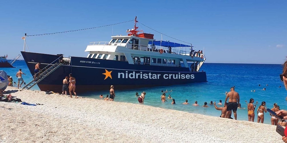 A beach with a large cruise ship docked, people swimming in the water, and a clear blue sky. 1