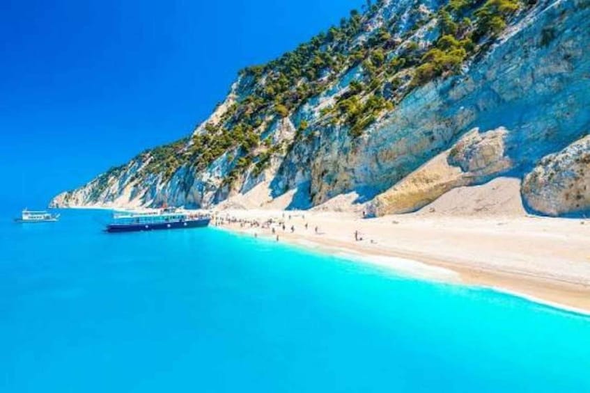 A coastal landscape with a clear blue sea, a sandy beach, and rocky cliffs. 4