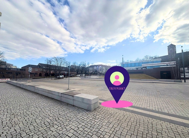 A paved plaza with a location marker, buildings, and a clear sky. 2