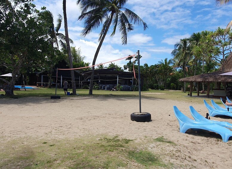 A beach volleyball court with net, palm trees, and blue lounge chairs. 4