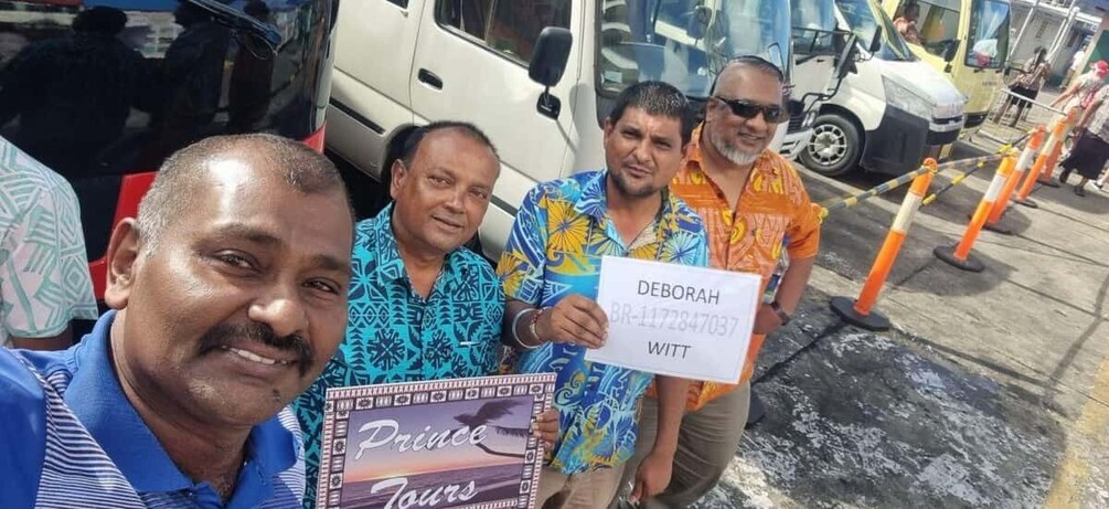 A group of people standing in front of a vehicle, holding a sign with a name and a number. 1