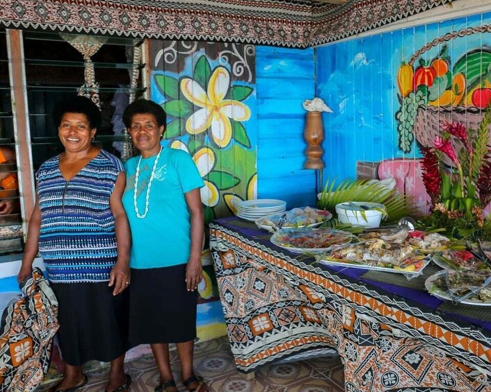 Two people standing in front of a table with food and a colorful mural. 3