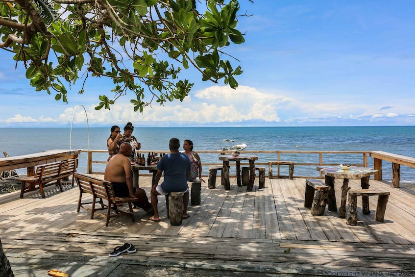 A wooden deck with people sitting at tables, overlooking a calm sea. 1