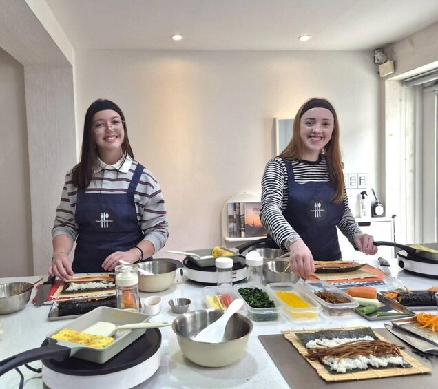 Two individuals preparing food, likely sushi, with various ingredients and tools on a table. 3