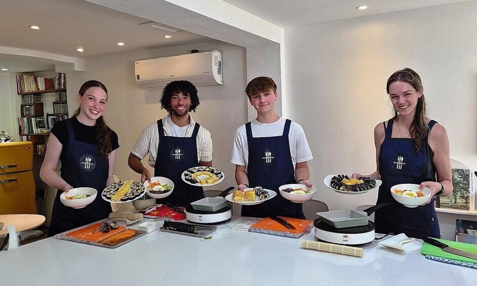 Four people in aprons holding plates of food in a kitchen. 4