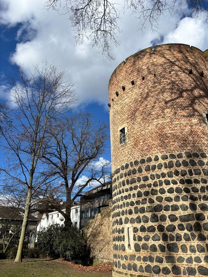 A brick tower with a stone base, surrounded by leafless trees and a clear sky. 2