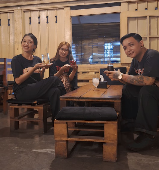 Four people seated at a wooden table with drinks, in a room with wooden walls and a window. 2