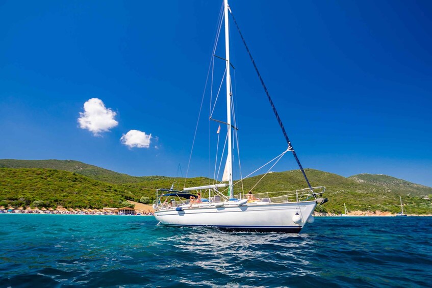 A sailboat on a calm sea with a beach and hills in the background. 5
