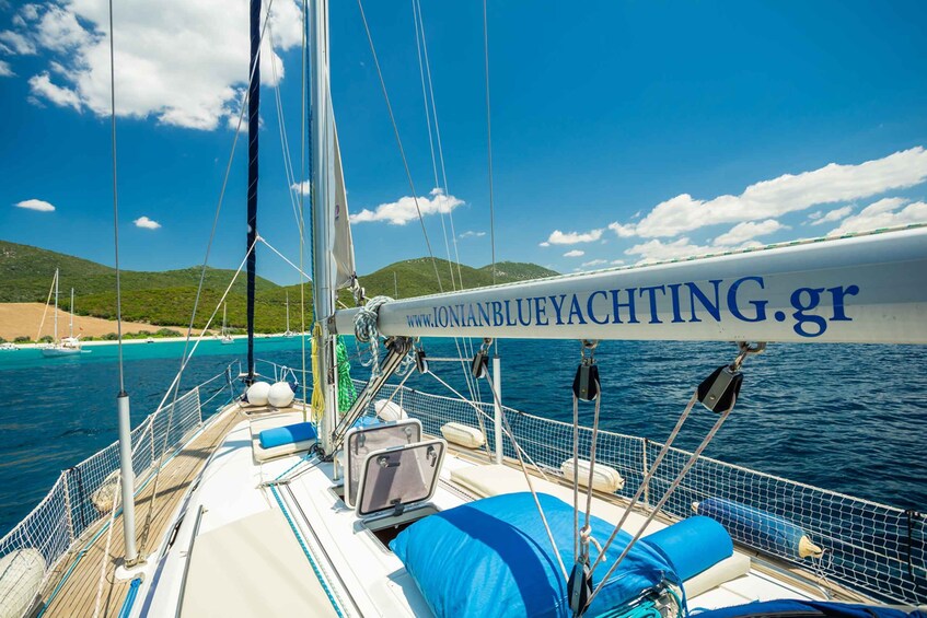 A sailboat with a mast and rigging, a cabin with a window, and a view of the sea and a coastline with hills. 1