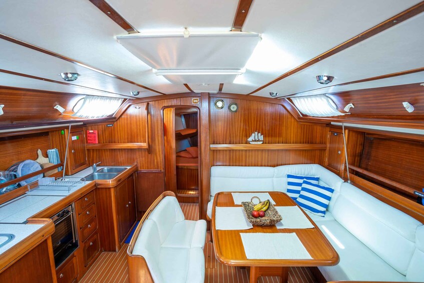 A well-lit, wooden interior of a boat with a dining area, seating, and a small kitchen. 3