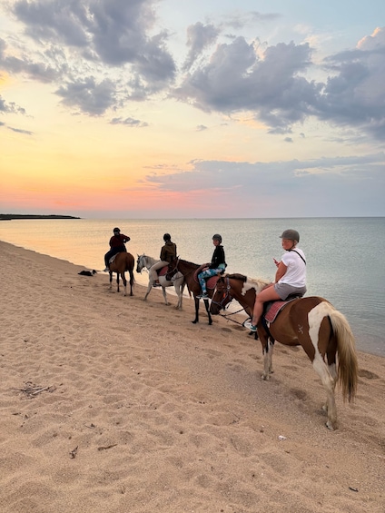A group of people riding horses along a beach at sunset. 5