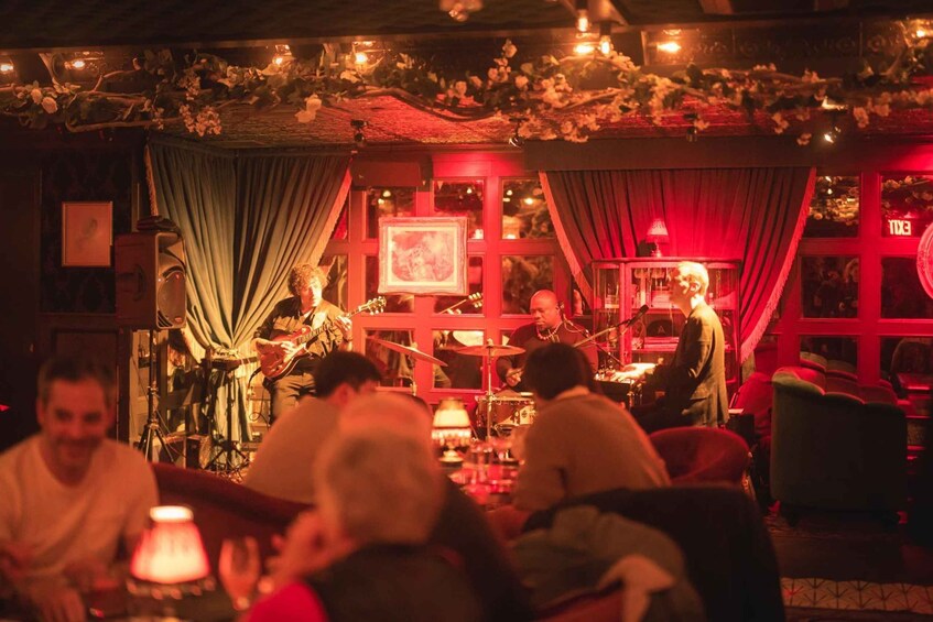 A band performing on stage with a red backdrop and audience seated in front. 3