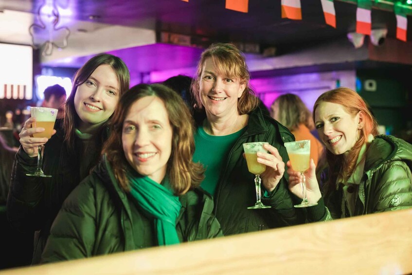 A group of people holding drinks in a bar with colorful lights in the background. 5