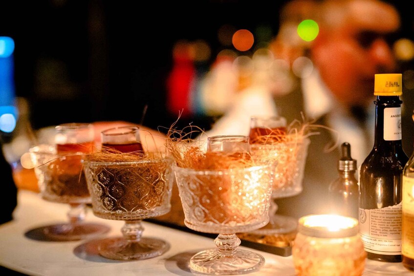 A bar setting with glasses of drinks, a bottle of Angostura bitters, and a candle. 2