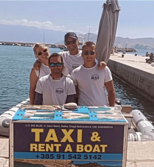 A group of people standing by a sign advertising a taxi and boat rental service. 4