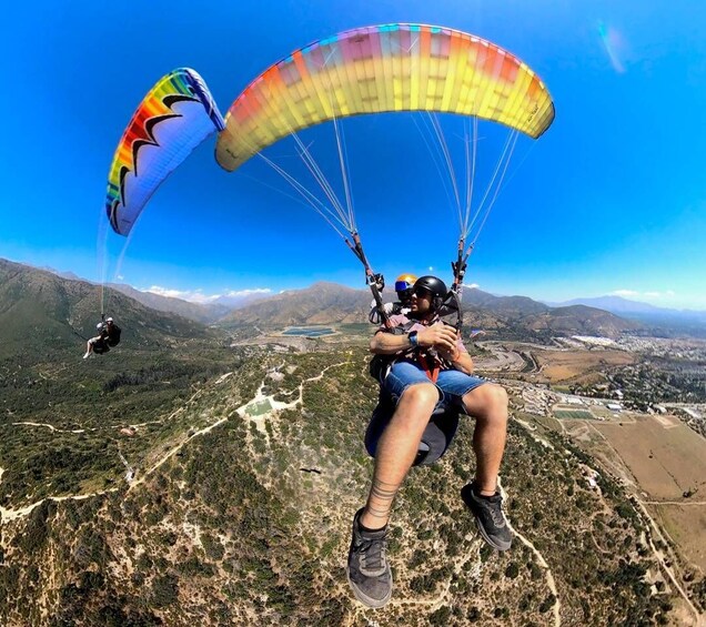 Two paragliders with colorful canopies flying over a mountainous landscape. 1