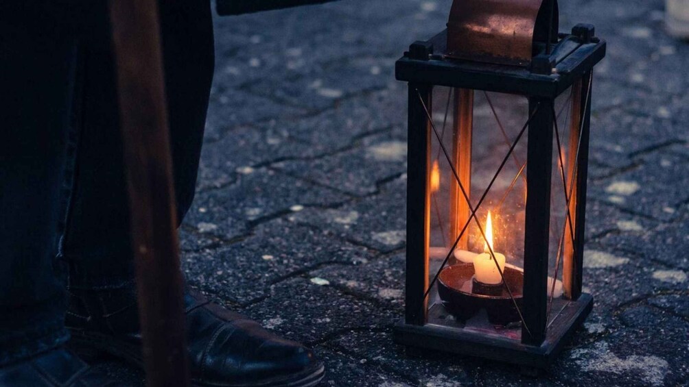 A person standing next to a lit lantern on a cobblestone street. 5