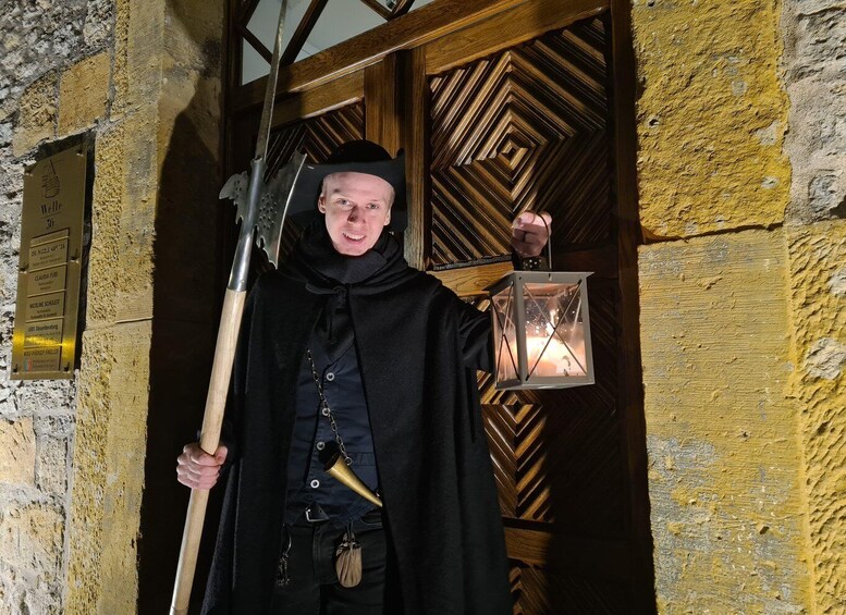 A person in a black cloak holding a lantern and a pitchfork. 1