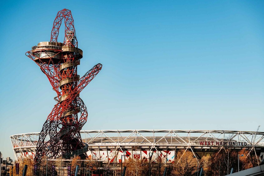 A large, red and black metal structure with a complex geometric design, likely a part of a stadium or sports facility, with a clear blue sky in the background. 2