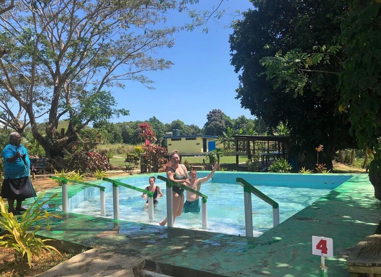 A swimming pool with people in it, surrounded by trees and a building in the background. 4