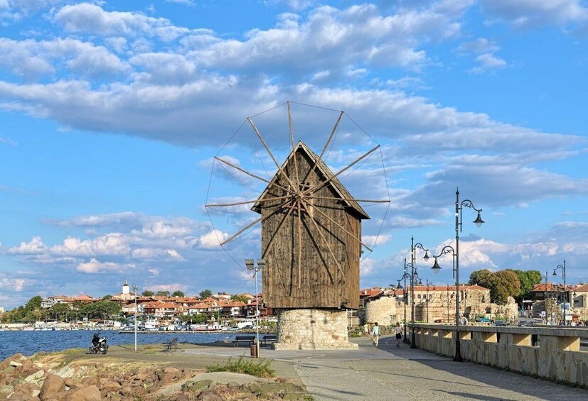 A traditional wooden windmill by a waterfront, with a stone base, and a townscape in the background. 2