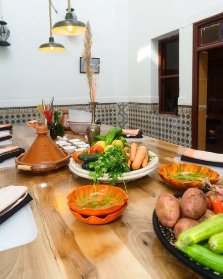 A wooden table with various dishes of vegetables, a terracotta pot, and a hanging light fixture. 3