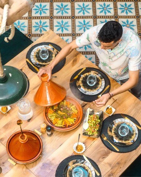 A person preparing a meal with a tagine on a wooden table. 2