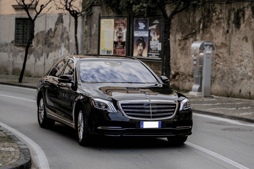 A black Mercedes-Benz car driving on a city street. 1