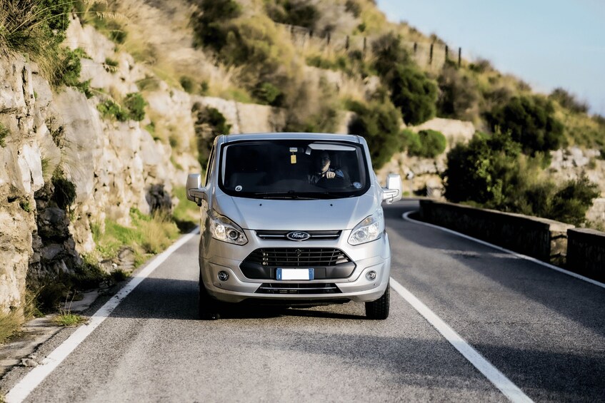 A silver Ford Focus driving on a winding mountain road with rocky cliffs on one side and greenery on the other. 2