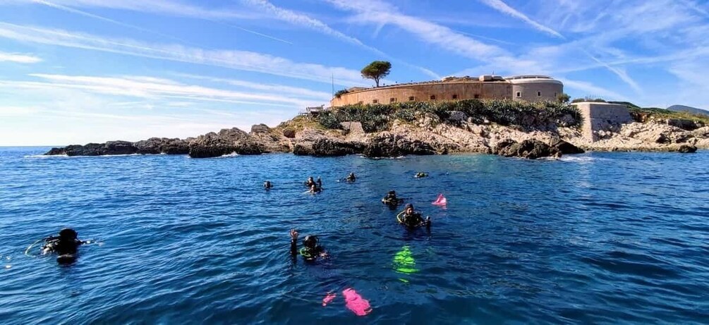 Divers in the water with a historic building on a rocky outcrop in the background. 3