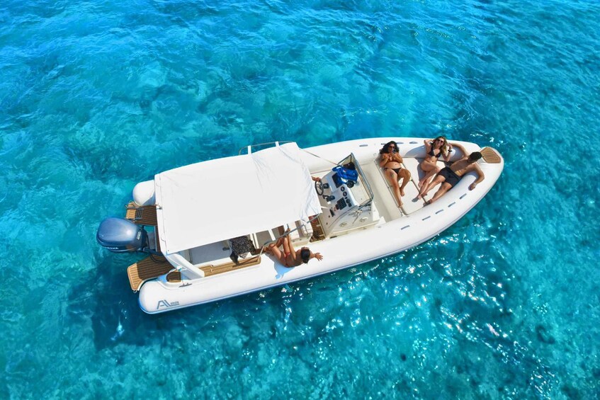 A white motorboat with a canopy, two people sunbathing, and clear turquoise water. 1