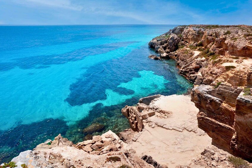 A coastal landscape with clear blue waters, rocky cliffs, and remnants of ancient ruins. 3