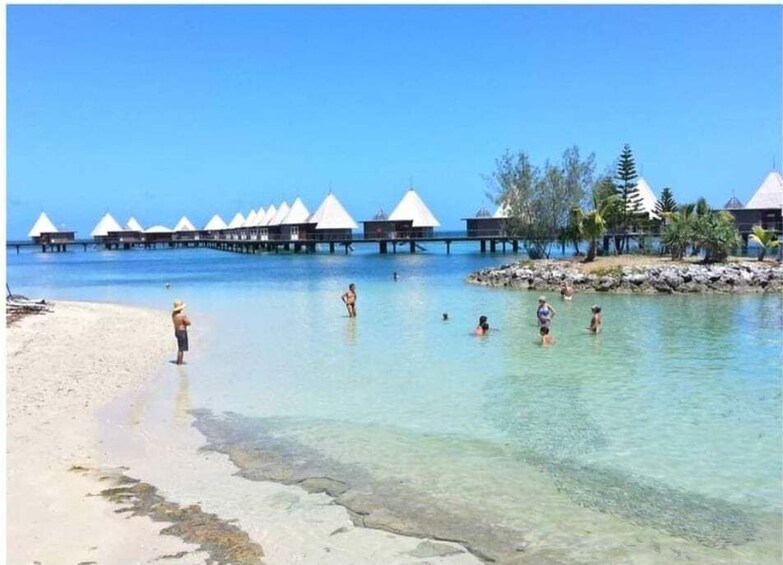 A beach with clear water, people swimming, and overwater bungalows. 4